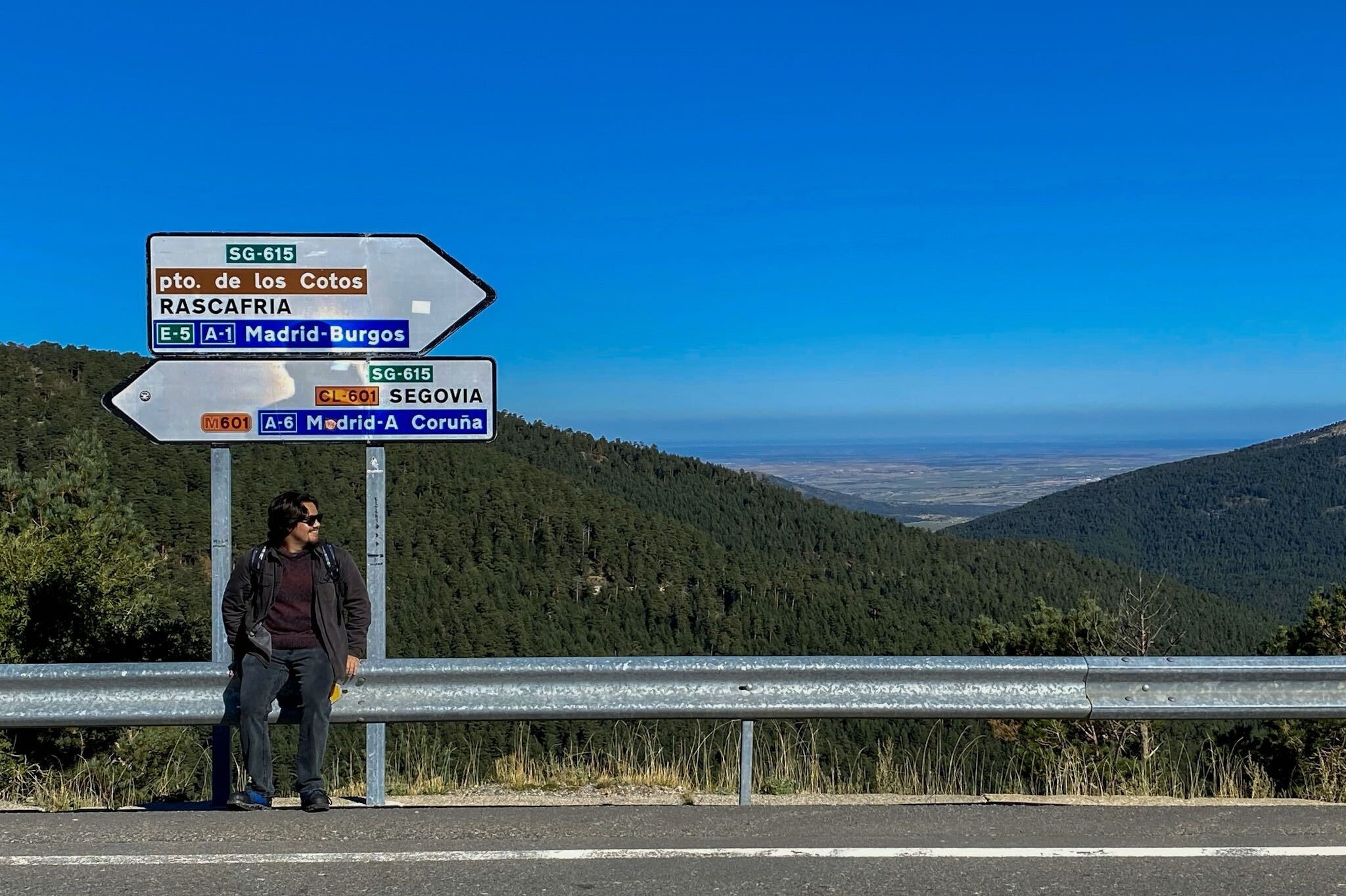 A student sitting on a guardrail with a roadside in Spanish behind him.